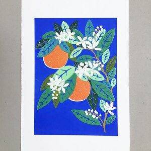 May include: A print of an orange tree with white blossoms and two orange fruits on a bright blue background.