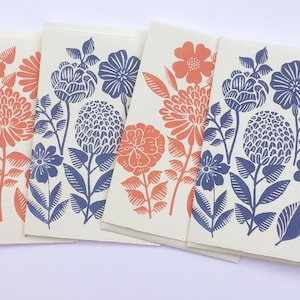 May include: Four cream-colored greeting cards with floral designs in coral and navy blue. The cards feature various flower illustrations, including chrysanthemums and other stylized blooms, with leaves and stems. The cards are stacked slightly, showcasing the designs.