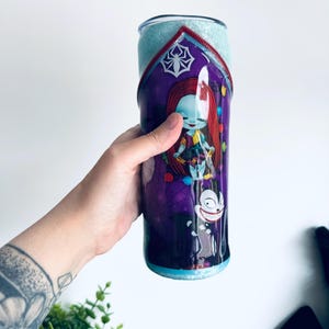 Puede incluir: Un vaso morado y azul con una imagen de dibujos animados de Sally de Pesadilla antes de Navidad. El vaso tiene un acabado brillante y un dise&ntilde;o de cremallera roja. El dise&ntilde;o incluye una telara&ntilde;a y un personaje de dibujos animados.