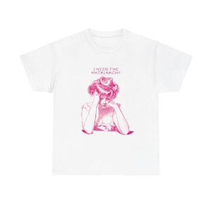 Könnte beinhalten: Weißes T-Shirt mit einer rosa Grafik einer Frau und dem Text "I NEED THE MATRIARCHY". Die Illustration zeigt eine Frau mit dem Kopf in den Händen. Das T-Shirt hat einen Rundhalsausschnitt.