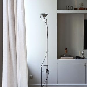 May include: A black floor lamp with a silver shade and a unique design. The lamp is in a room with white walls and a white curtain.