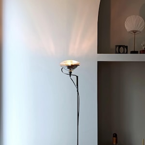 May include: A black floor lamp with a silver, round lampshade. The lamp is casting a light pattern on the wall behind it.