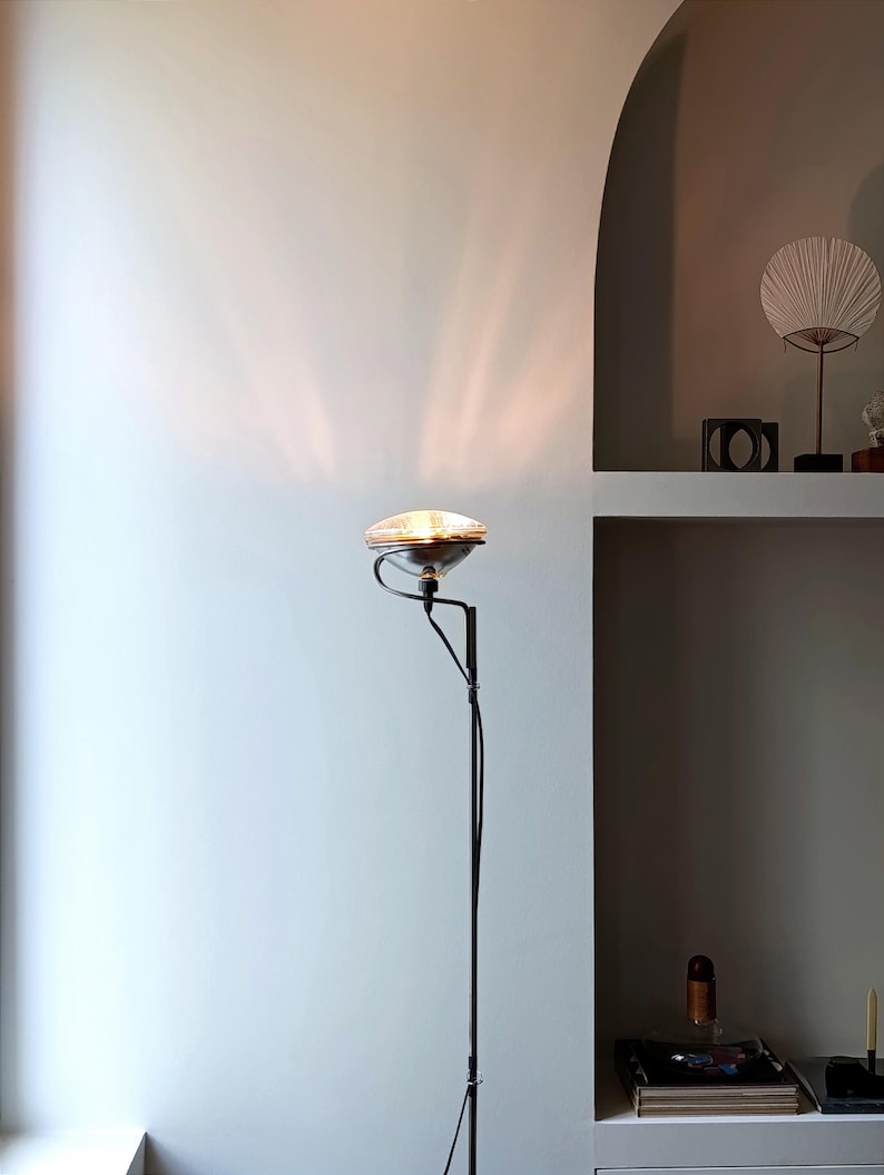 May include: A black floor lamp with a silver, round lampshade. The lamp is casting a light pattern on the wall behind it.