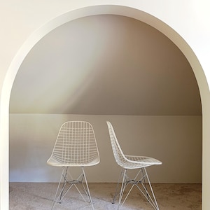 May include: Two white wire chairs with chrome legs are positioned in front of an arched doorway. The chairs are in a room with beige carpet.