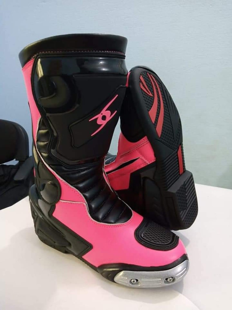 May include: Pink and black motorcycle boots with silver accents. The boots have a black leather upper with a pink leather lower section. The boots have a black zipper on the side and a black strap across the top.