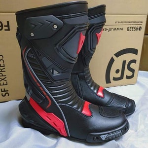 May include: A pair of black leather motorcycle boots with red accents and a gray and black design. The boots have a zipper on the side and a logo on the toe.