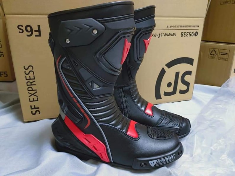 May include: A pair of black leather motorcycle boots with red accents and a gray and black design. The boots have a zipper on the side and a logo on the toe.