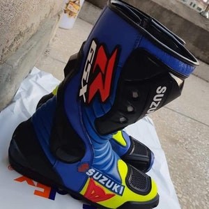 May include: Blue and yellow motorcycle boots with black accents and the word "Suzuki" printed on the side. The boots have a red "Z" logo and the text "GSX-R" on the side.