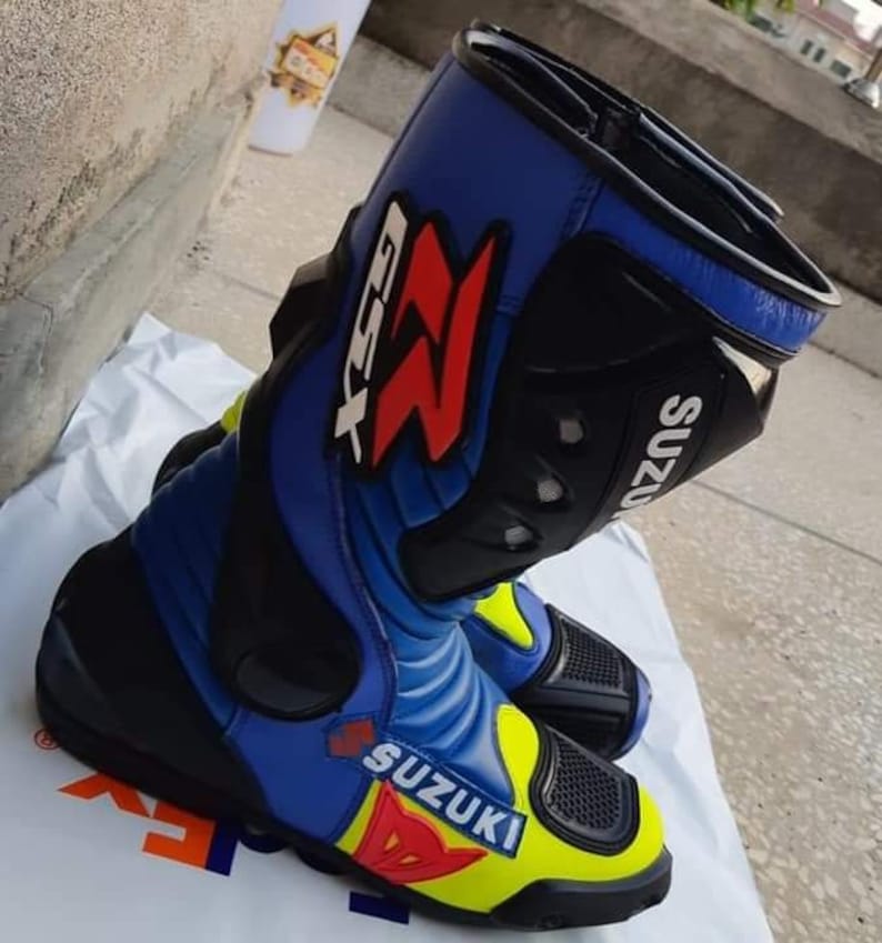 May include: Blue and yellow motorcycle boots with black accents and the word "Suzuki" printed on the side. The boots have a red "Z" logo and the text "GSX-R" on the side.
