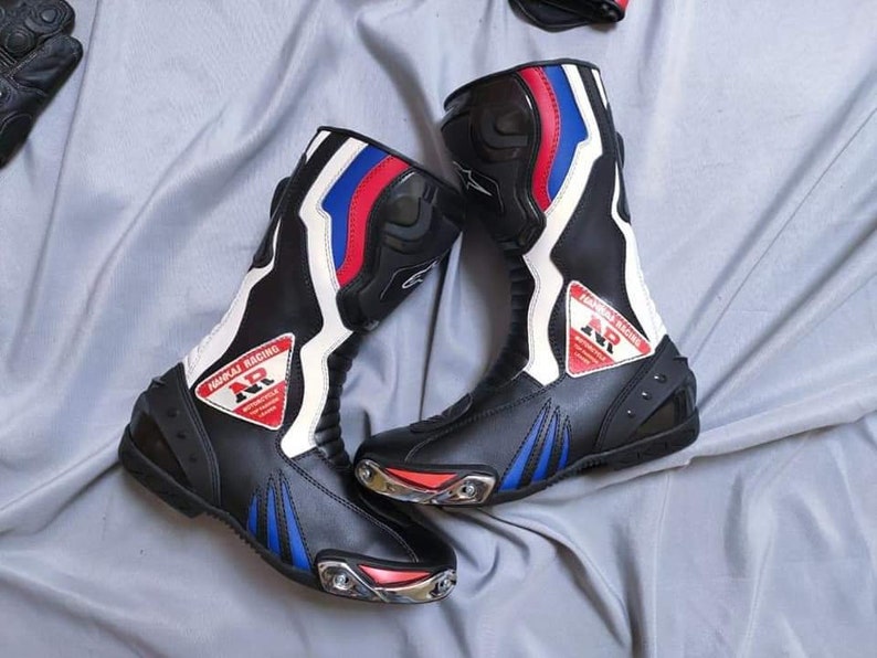 May include: A pair of black leather motorcycle boots with white, red, and blue accents. The boots have a  "MORRJAJ RACING" logo with the letters "NR" in a triangle.