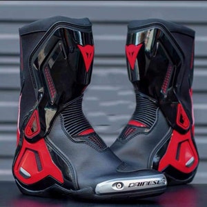 May include: A pair of black and red motorcycle boots with a silver Dainese logo on the side. The boots have a high top and a sporty design.