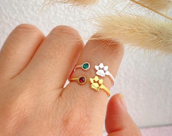 May include: Two gold and silver rings with paw print designs. The gold ring has a red gemstone and the text "Family" inscribed on the paw print. The silver ring has a green gemstone and the text "Limmy" inscribed on the paw print.