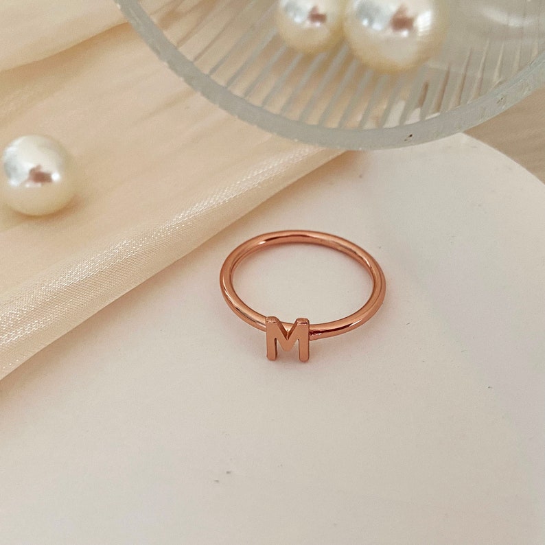 Peut inclure: Une bague en or rose avec la lettre "M" dessus.