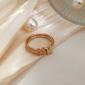 Peut inclure: Une bague en or et or rose avec les lettres MK dessus. La bague est sur un fond de tissu blanc.