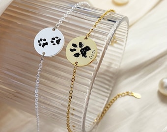 May include: Two silver and gold bracelets with paw print charms. The gold charm has the name "OzZy" engraved on it.