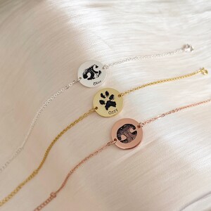 Puede incluir: Tres pulseras de plata, oro y oro rosa con dijes redondos que muestran huellas de patas y los nombres "Chico", "Ozzy" y un nombre ilegible.