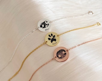 May include: Three silver, gold, and rose gold bracelets with round charms featuring paw prints and the names "Chico", "Ozzy", and an unreadable name.