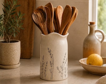 Op de afbeelding: Een crèmekleurige keramische keukengerei-houder met een fijne zwarte lijntekening van lavendeltakjes, gevuld met diverse houten lepels. De houder staat op een aanrecht naast een kleine plant in pot, een oliekruikje en een citroen.