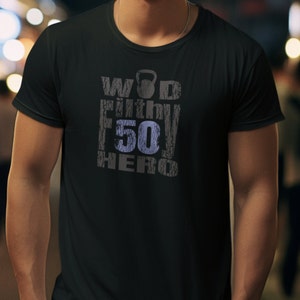 May include: Black t-shirt with the text "WOD Fit 50 Hero" in a distressed, gray and blue font. The design includes a kettlebell graphic above the text. The shirt is a crew neck style.