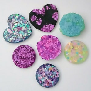 Pode incluir: Sete ornamentos à base de resina com glitter embutido na resina. Os ornamentos têm a forma de corações e círculos. As cores dos ornamentos são preto, rosa, azul, verde e branco.