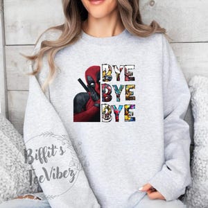 May include: A gray sweatshirt with a graphic of Deadpool's head and the words "Bye Bye Bye" in colorful letters. The graphic is made up of various comic book characters.