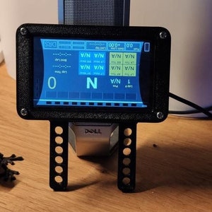May include: A black and blue digital display with a black frame and stand. The display shows the text "TROC" and "DRS" and a series of numbers and letters. The display is mounted on a black stand with a series of holes.