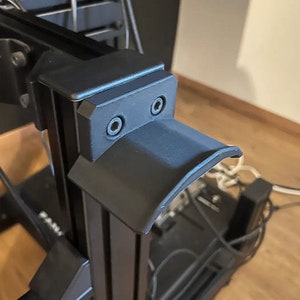May include: Black 3D printer part with a curved design and two screw holes. The part is made of plastic and has a matte finish.