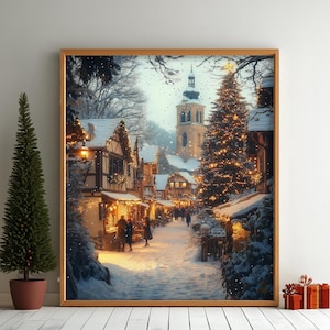 May include: A framed print depicts a snowy Christmas village scene. The artwork showcases a street lined with buildings, a church tower, and a decorated Christmas tree. The image is framed in a light wood, with a small potted tree and wrapped gifts in the foreground.