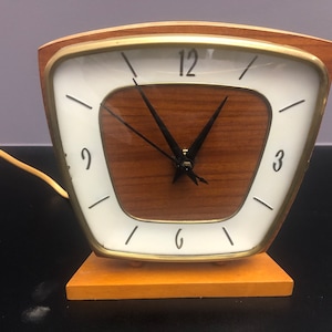 May include: A vintage wooden clock with a white face and black hands. The clock has a gold trim and is on a wooden base.