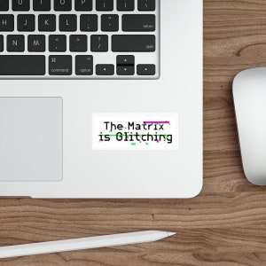May include: A white sticker with the text "The Matrix is Glitching" in black with a glitching effect in green, pink, and blue.