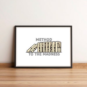 May include: A black framed print with a white background. The print features a line of dominoes falling over with the text "METHOD TO THE MADNESS" below.
