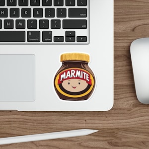 May include: A sticker of a cartoon jar of Marmite with a smiling face. The jar is brown with a yellow lid and the word "Marmite" is printed in red letters on the label.