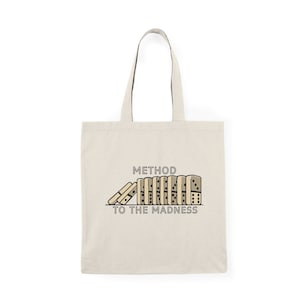 May include: Beige tote bag with black handles. The bag features a graphic of dominoes with the text "METHOD TO THE MADNESS" in black. The dominoes are beige with black dots and outlines.