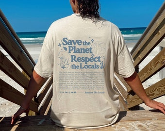 Puede incluir: Camiseta beige con el texto "Save the Planet Respect the Locals" en azul claro. La parte posterior de la camiseta presenta ilustraciones de un oso polar, un globo terráqueo y otros gráficos. La persona está sentada en escalones de madera con el mar y el cielo de fondo.