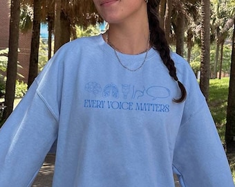 May include: A light blue sweatshirt with the text "Every Voice Matters" and a graphic of a microphone, a hand with a raised fist, a heart, and a speech bubble.