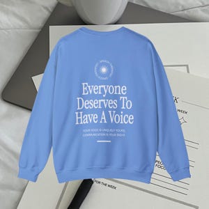 Puede incluir: Una sudadera azul claro con un estampado gr&aacute;fico blanco que dice "Everyone Deserves To Have A Voice". El gr&aacute;fico tambi&eacute;n incluye un c&iacute;rculo con un dise&ntilde;o de sol radiante y las palabras "Speech The Power".