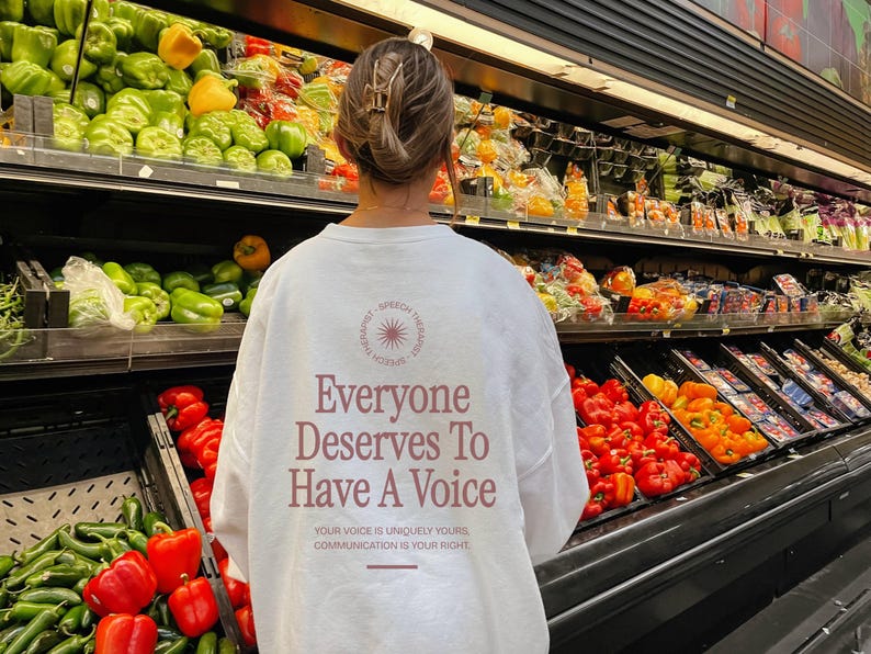 Puede incluir: Sudadera blanca de manga larga con el texto "Everyone Deserves To Have A Voice" en letras rosas. El texto est&aacute; rodeado de un c&iacute;rculo con un gr&aacute;fico de sol. El texto debajo del c&iacute;rculo dice "Your voice is uniquely yours, communication is your right."
