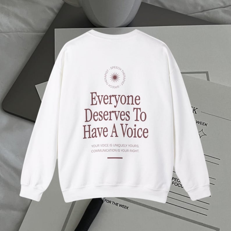 Puede incluir: Sudadera blanca de manga larga con un estampado gr&aacute;fico marr&oacute;n que dice "Everyone Deserves To Have A Voice." El gr&aacute;fico tambi&eacute;n incluye un c&iacute;rculo con un dise&ntilde;o de sol radiante y las palabras "Speech Therapist."