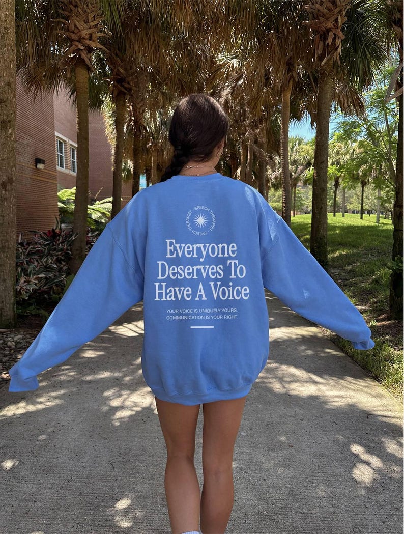 Puede incluir: Una sudadera azul claro con el texto "Everyone Deserves To Have A Voice" y el texto "Your voice is uniquely yours. Communication is your right." impreso en la parte posterior.