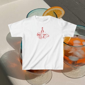 May include: White t-shirt with a red illustration of a bottle of wine, a glass of wine, grapes, and a piece of cheese.