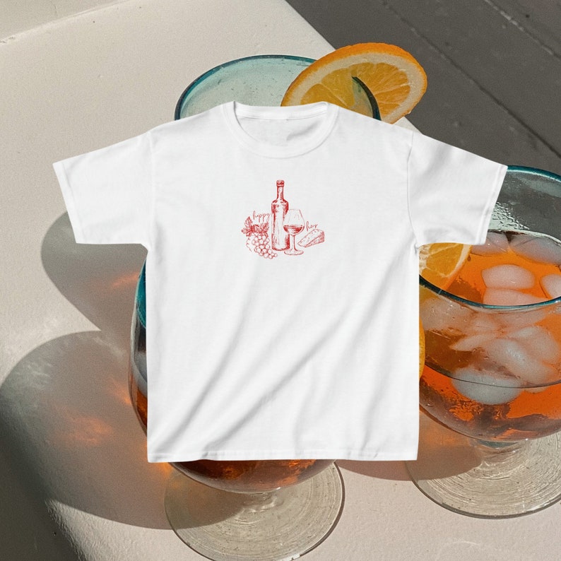 May include: White t-shirt with a red illustration of a bottle of wine, a glass of wine, grapes, and a piece of cheese.