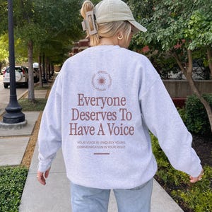 Puede incluir: Una sudadera gris con el texto "Everyone Deserves To Have A Voice" impreso en la espalda. El texto est&aacute; en marr&oacute;n e incluye la frase "Your voice is uniquely yours, communication is your right."