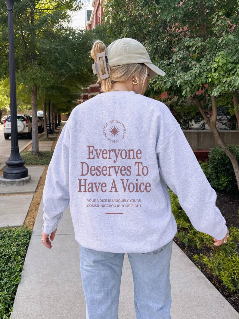 Puede incluir: Una sudadera gris con el texto "Everyone Deserves To Have A Voice" impreso en la espalda. El texto est&aacute; en marr&oacute;n e incluye la frase "Your voice is uniquely yours, communication is your right."
