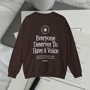Puede incluir: Una sudadera de manga larga marr&oacute;n con el texto "Everyone Deserves To Have A Voice" impreso en la espalda. El texto est&aacute; rodeado de un c&iacute;rculo con las palabras "Speech Therapist" impresas alrededor.