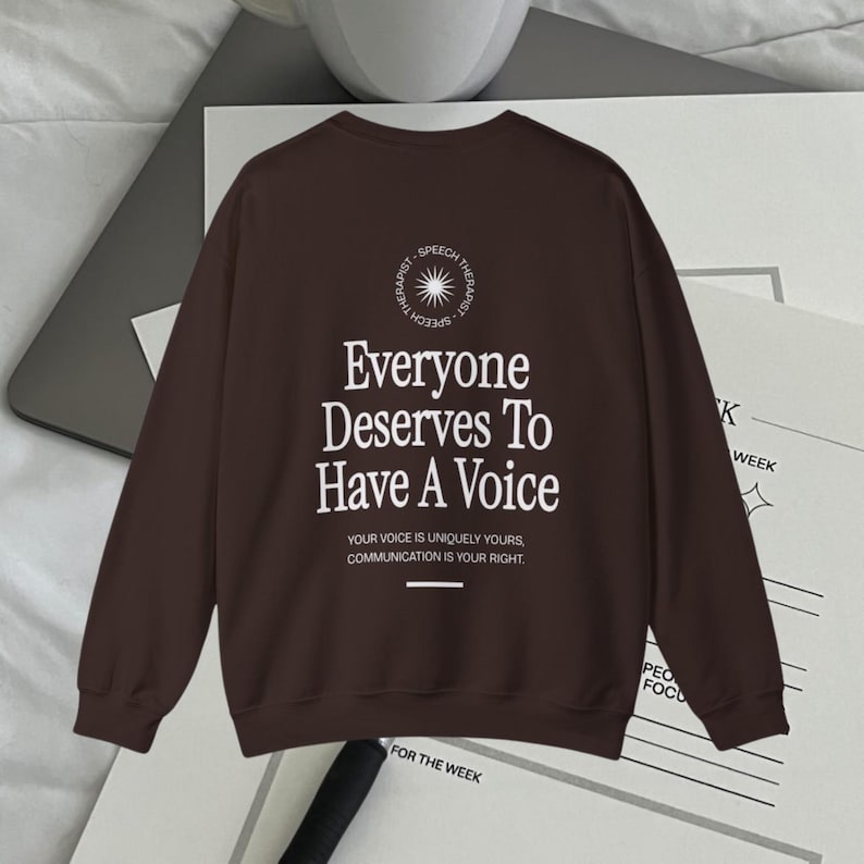 Puede incluir: Una sudadera de manga larga marr&oacute;n con el texto "Everyone Deserves To Have A Voice" impreso en la espalda. El texto est&aacute; rodeado de un c&iacute;rculo con las palabras "Speech Therapist" impresas alrededor.