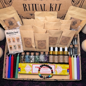 May include: A brown wooden box filled with various items for a ritual kit. The box contains small brown paper bags, glass bottles, candles, crystals, incense, and a bracelet. The box is labelled "Ritual Kit" and has the text "The Moonchild Tarot UK" on the top.
