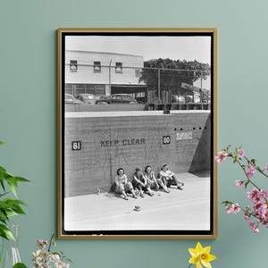 May include: Black and white photograph of five women sitting on a concrete wall. The wall has the words "Keep Clear" and "No Smoking Within 50 Feet" written on it. The women are wearing dresses and skirts. The photo was taken in the 1940s.