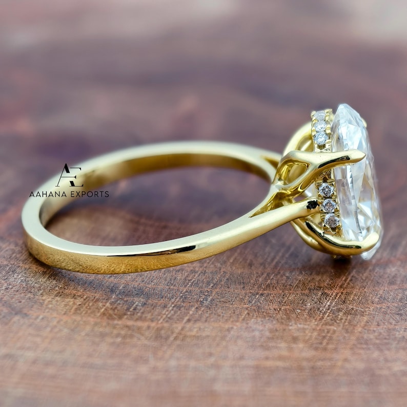 May include: A gold ring with a large, clear, oval-cut gemstone. The ring features a delicate band and a halo of smaller stones around the main gem. The ring is set against a wooden surface, with the text "AAHANA EXPORTS" visible.