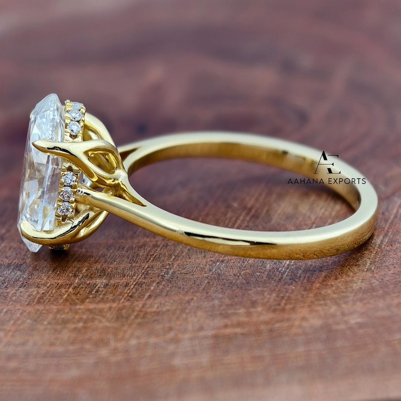 May include: A close-up of a gold ring with a large, clear, oval-cut gemstone. The ring has a delicate band and is set with smaller accent stones around the main stone. The ring is on a wooden surface. The text "AAHANA EXPORTS" is visible.