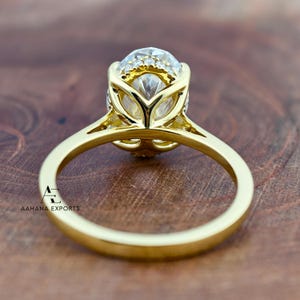 May include: A gold ring with a large, oval-cut gemstone, surrounded by smaller stones. The ring's band is smooth and polished, and the setting has a decorative design. The ring is set against a wooden background.